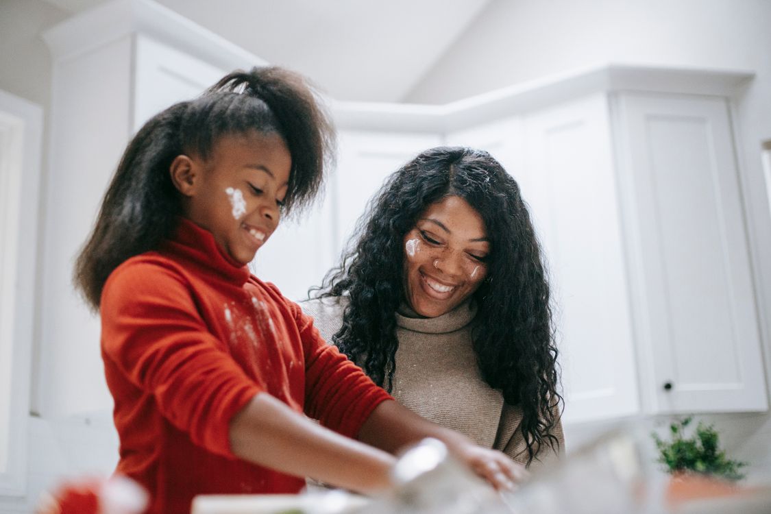 A mother and daughter smiling while baking together in a flour-dusted kitchen