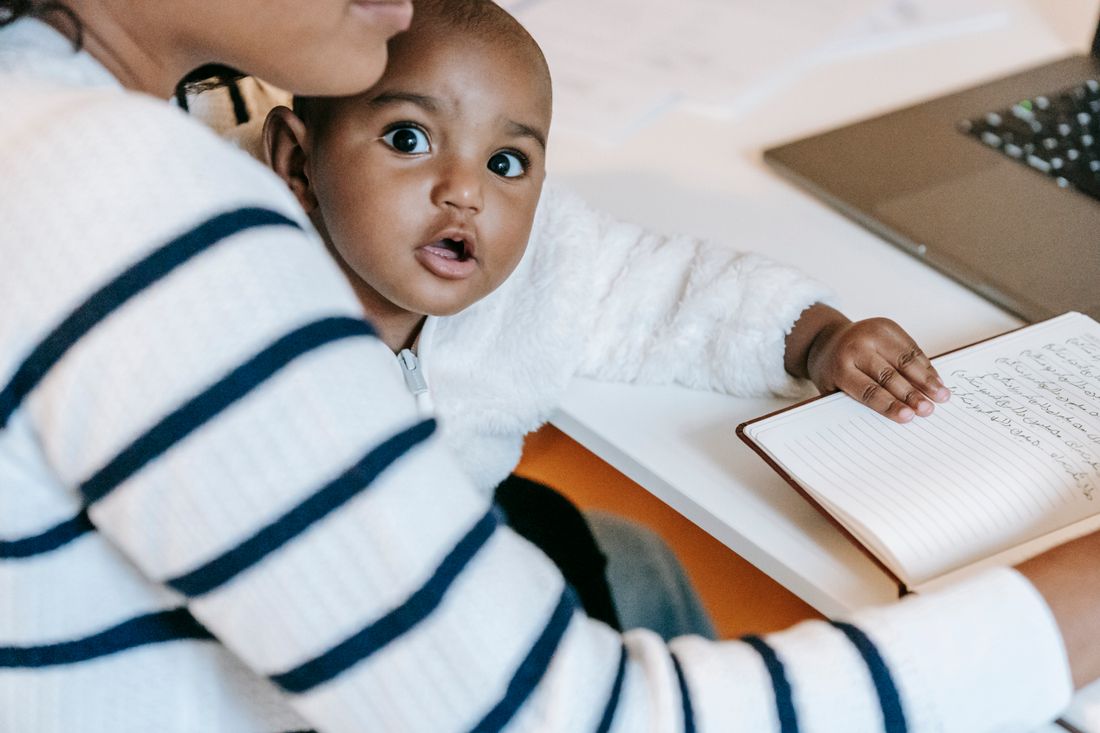 A parent writing in a notebook with a young child on their lap.
